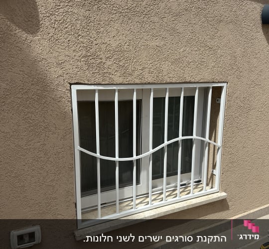 חלון עם סורגים לבנים על קיר חום